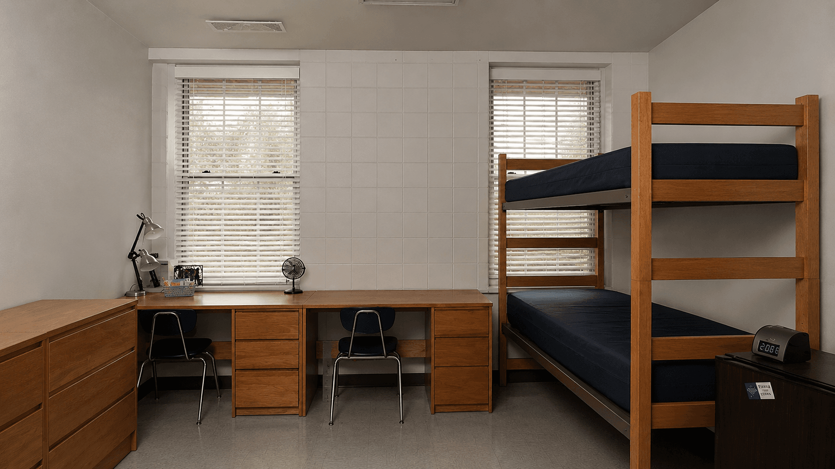 The bare school-issued NYC double dorm room with a wooden bunk bed, two desks, and empty walls